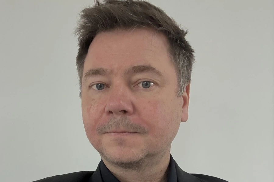 middle aged man with dark hair in black shirt with light grey wall in background
